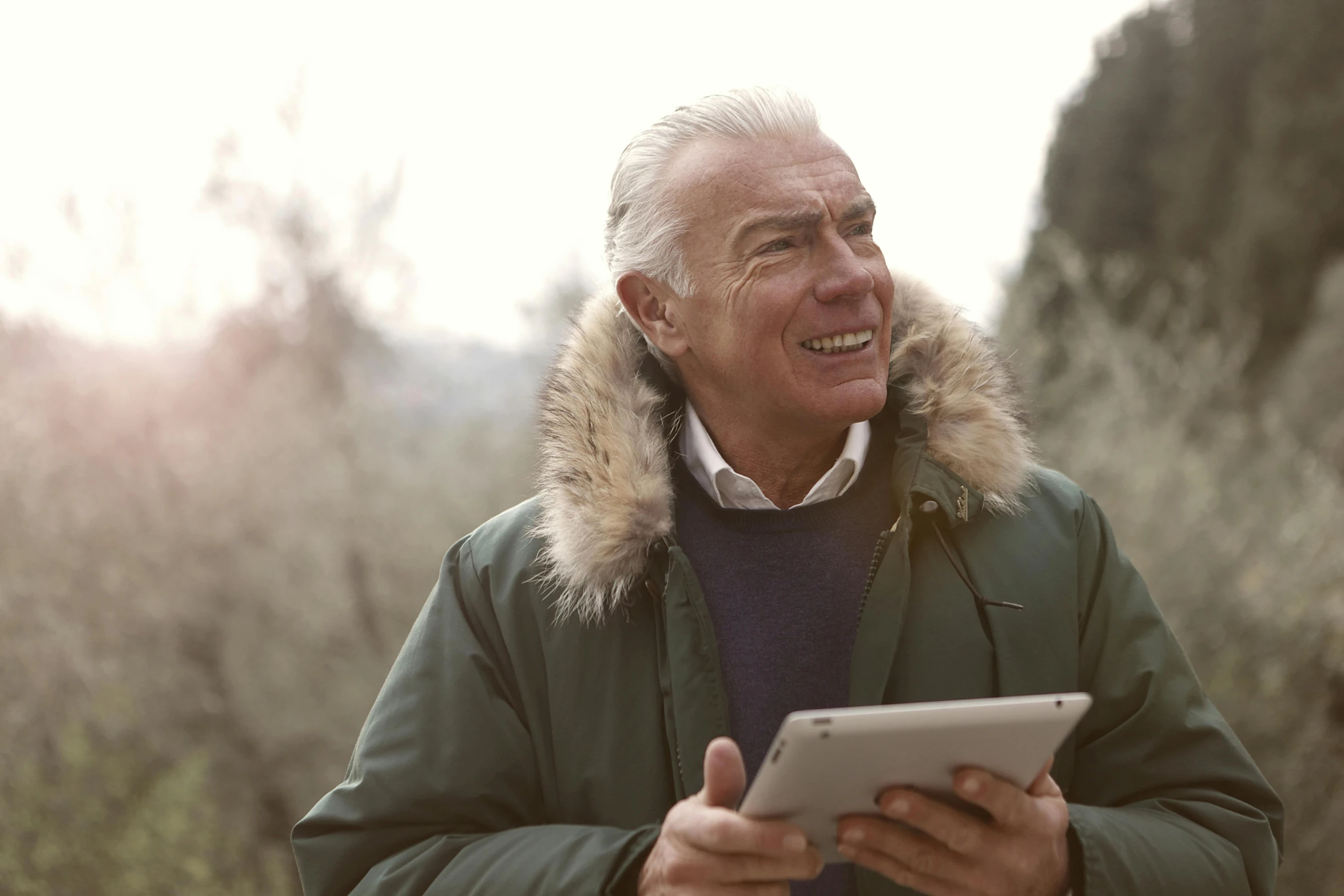 a man in a parka using a tablet computer, a portrait, by Julian Allen, pexels, white haired, a still of a happy, hills in the background, a wooden