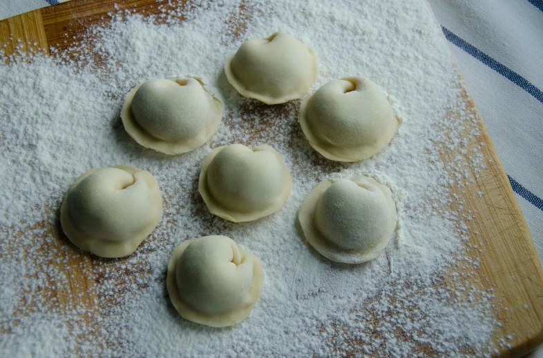 a wooden cutting board topped with dumplings covered in powdered sugar, inspired by Károly Patkó, 6 pack, italian renaissance workshop, folds, holes
