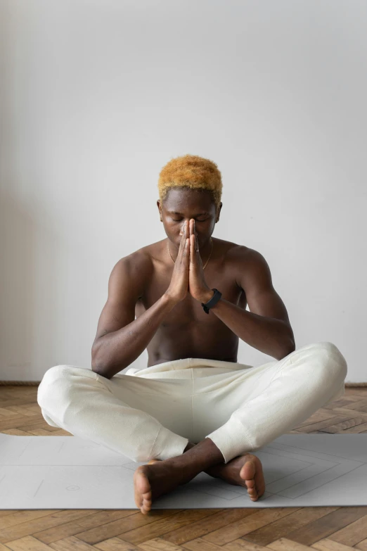 a man in white pants sitting on a yoga mat, trending on unsplash, renaissance, short blonde afro, praying posture, brown skinned, a blond