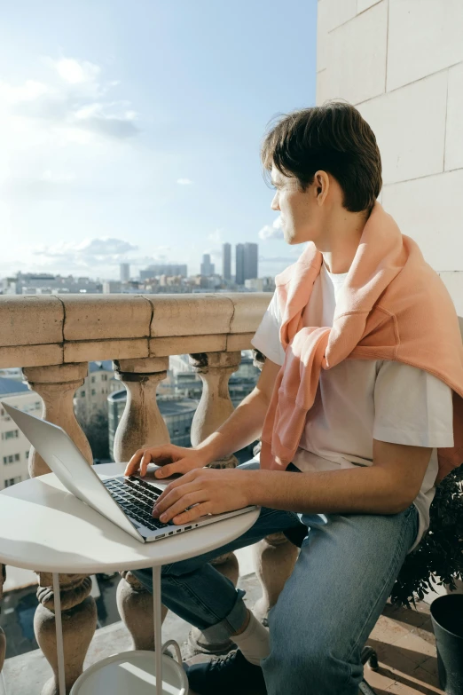 a man sitting on a balcony using a laptop, trending on pexels, happening, wearing a scarf, an epic non - binary model, russian academic, city backdrop