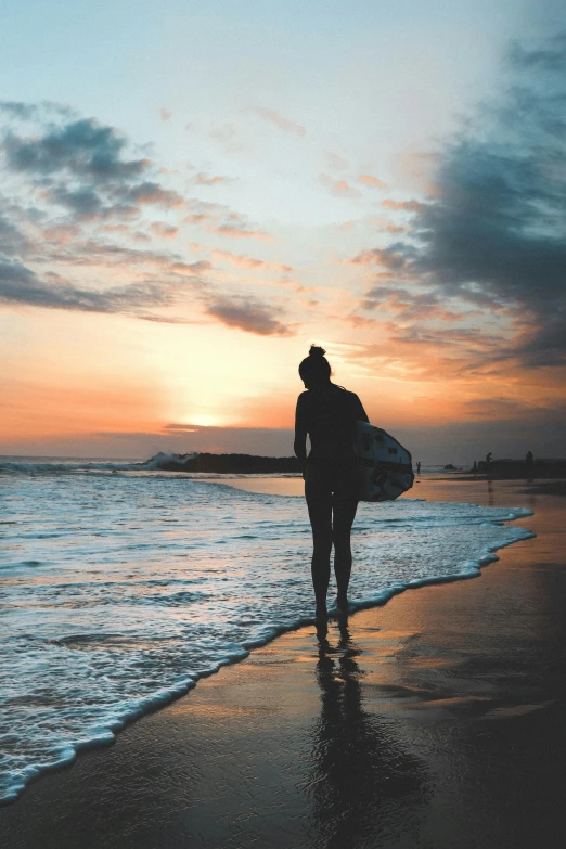 a person standing on a beach holding a surfboard, during a sunset