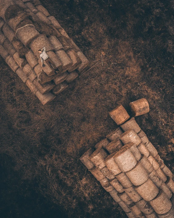 a couple of benches sitting on top of a dirt field, an album cover, by Filip Hodas, unsplash contest winner, land art, bricks, top down view, sculpture made of piled stones, person in foreground