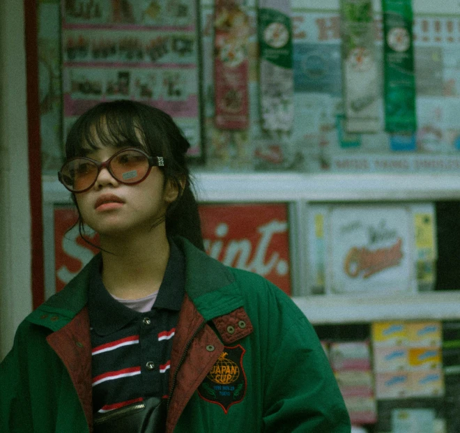 a woman standing in front of a store, inspired by Liam Wong, trending on pexels, girl wearing round glasses, green and red tones, movie shot, she wears a jacket