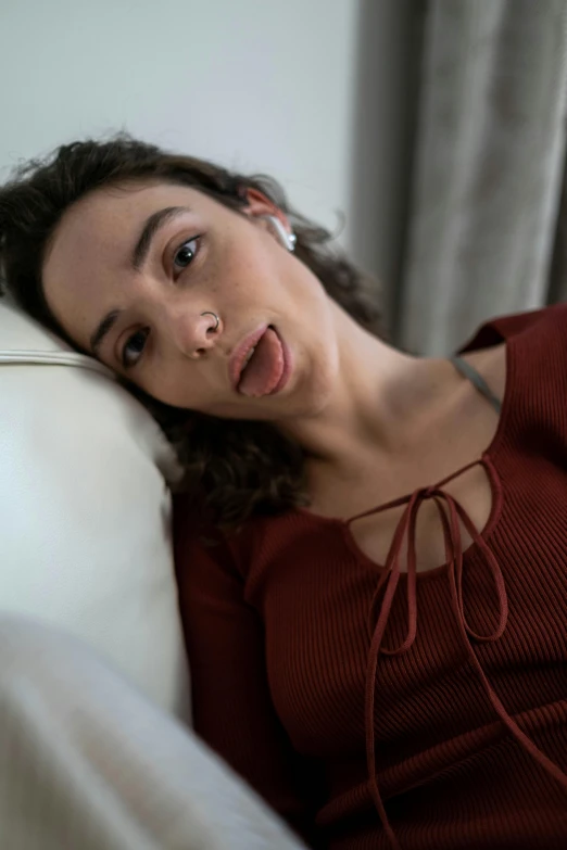 a woman laying on a couch with a remote in her hand, an album cover, inspired by Louis Le Nain, trending on pexels, photorealism, tongue out, oona chaplin, exhausted face close up, non binary model