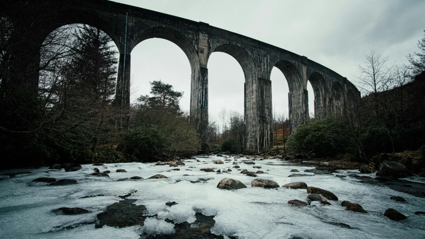 an old stone bridge spanning over a snow covered forest