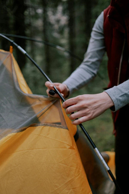 a person setting up a tent in the woods, up-close, less detailing, yellow, wire management