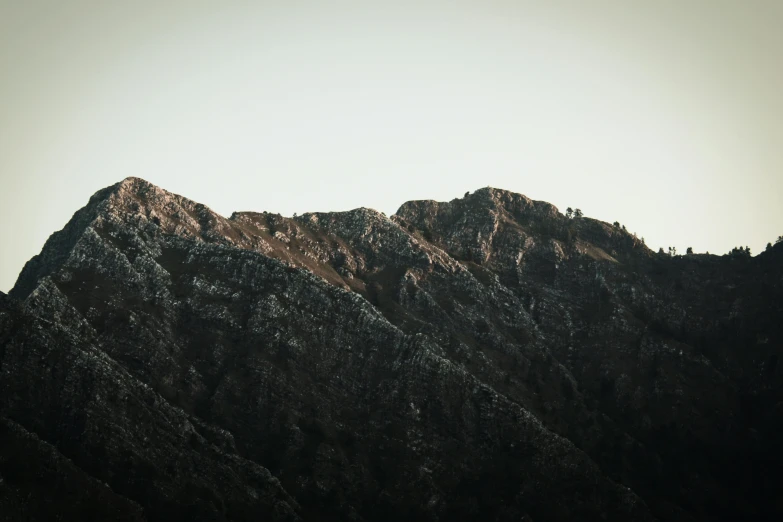 a mountainside mountain with dark vegetation and the sun peeking over