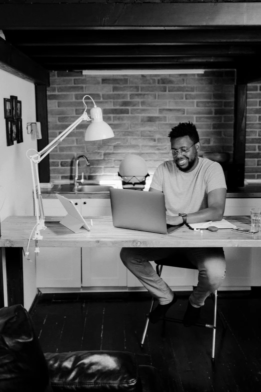 a man sitting at a desk with a laptop computer, a black and white photo, by Sam Charles, pexels contest winner, afro tech, standing upright, smiling man, male character