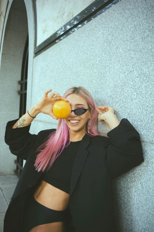 a woman with pink hair holding an orange in front of her face, a photo, inspired by Elsa Bleda, trending on pexels, lemon wearing sunglasses, belly button showing, black and yellow, maxim sukharev
