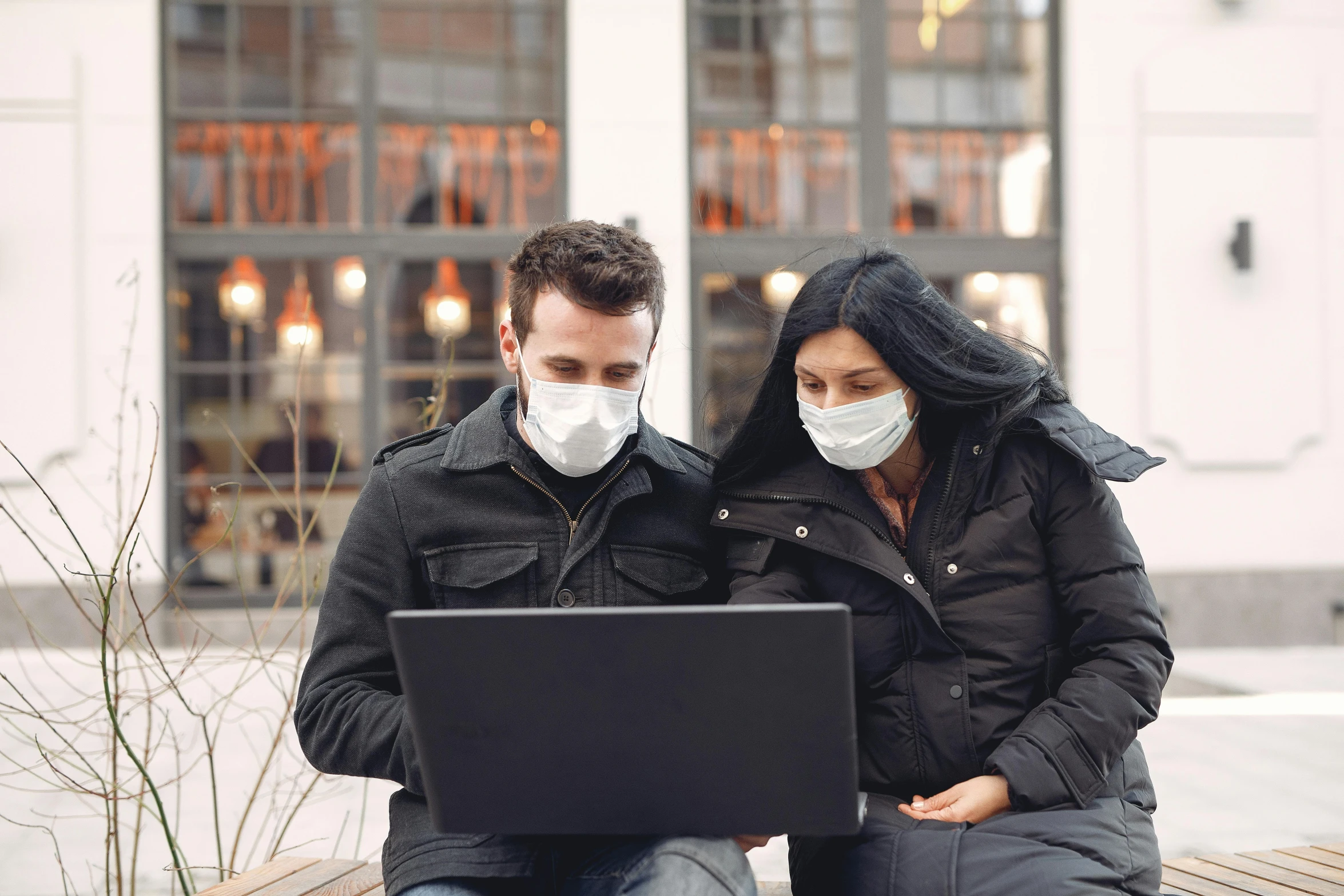 two people sitting on the bench with a laptop computer