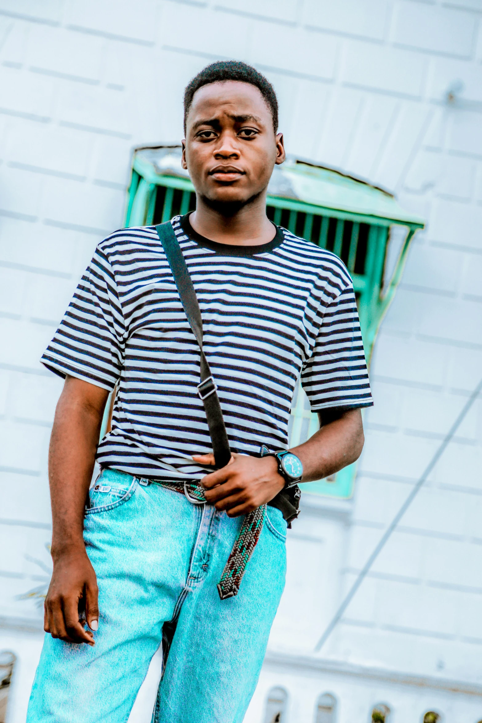 a man wearing blue pants and a striped t - shirt, holding his camera strap