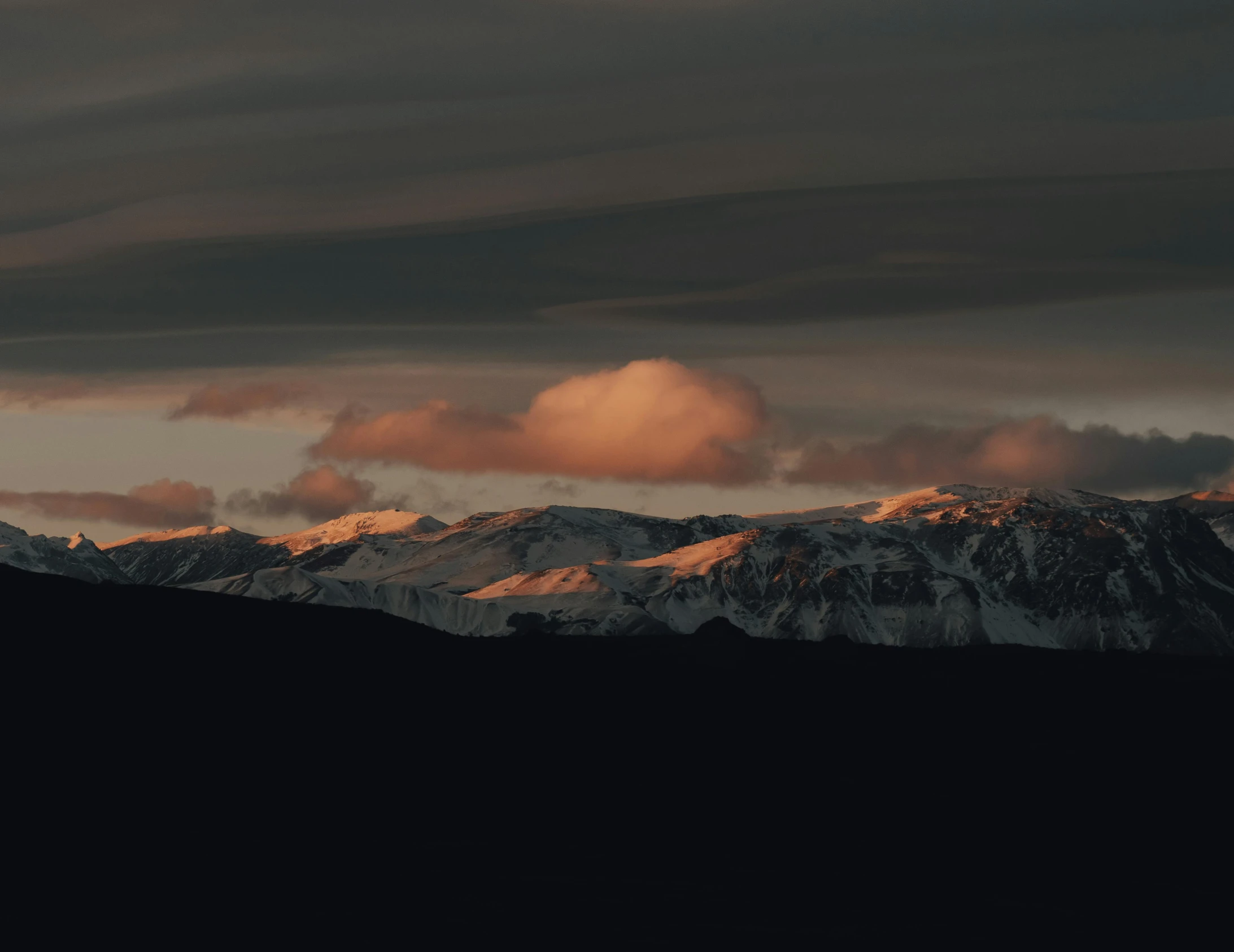 some dark clouds over some snow capped mountains