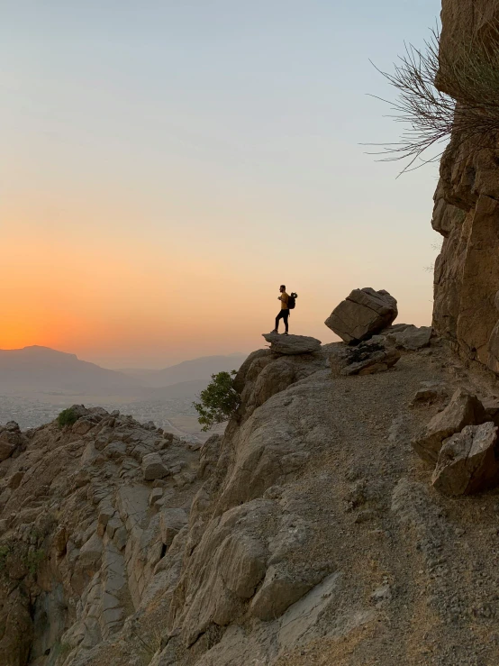 a person standing on top of a large rock, during a sunset, oman, solo hiking in mountains trees, behind the scenes