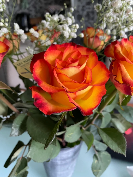 a close up of a vase of flowers on a table, up-close, red and orange colored, yellow rose, zoomed in