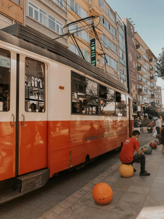 a red and white train on a city street, by Emma Andijewska, pexels contest winner, grey orange, turkey, panoramic shot, sitting down