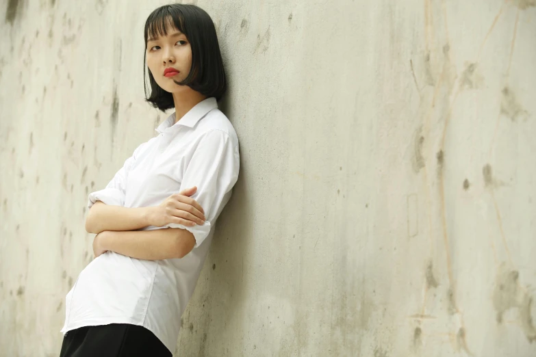 a woman leaning against a wall with her arms crossed, inspired by Zhou Wenjing, trending on pexels, minimalism, collared shirt, 奈良美智, frown fashion model, white