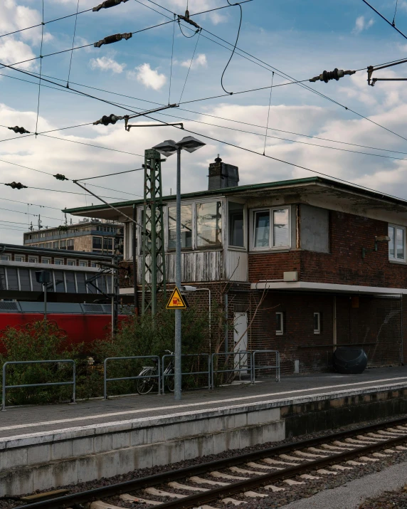 a train pulling into a train station next to a building, regionalism, overhead wires, transgender, documentary photo, thumbnail