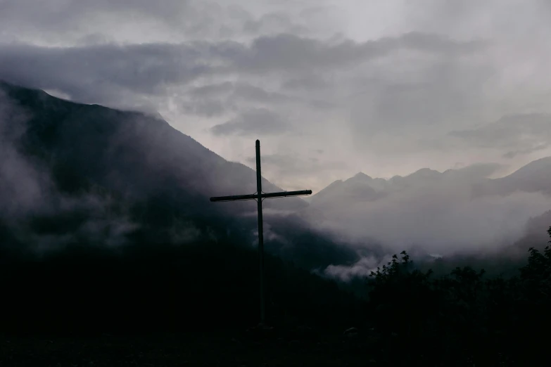 a crucifix stands against a background of mist, mountains and trees