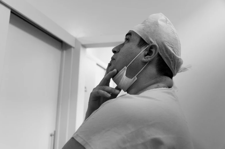 a black and white photo of a surgeon talking on a cell phone, by Adam Marczyński, unsplash, figuration libre, protruding chin, wearing a white bathing cap, looking to the right, surgery theatre