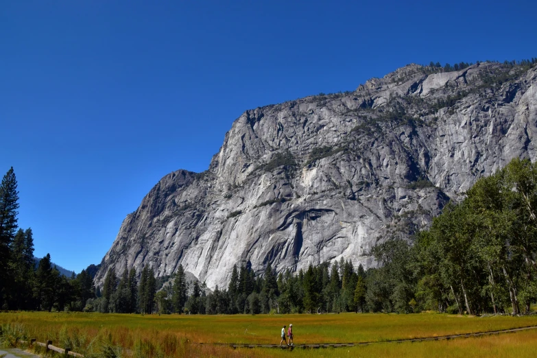 a person standing in a field with a mountain in the background, yosemite valley, clear blue skies, structural geology, nature photo