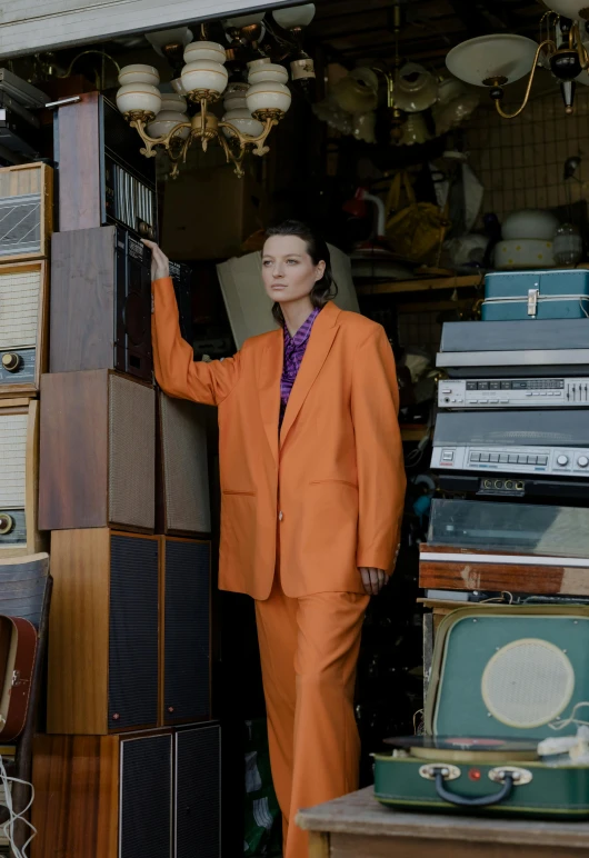 a woman in an orange suit standing in a garage, an album cover, unsplash, bauhaus, wearing a worn out brown suit, jodie foster, 15081959 21121991 01012000 4k, radios