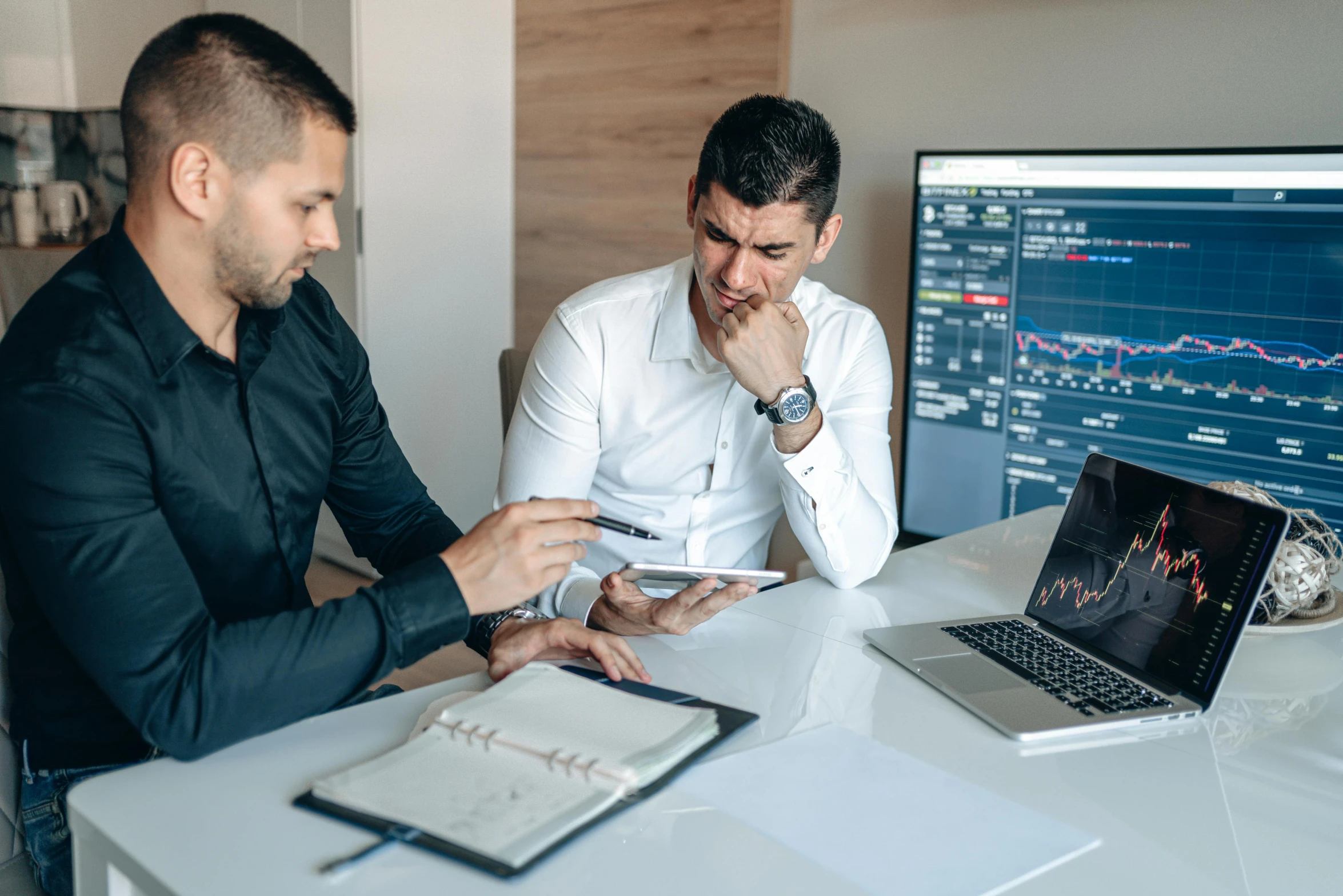 two men sitting at a table looking at a laptop, by Adam Marczyński, pexels contest winner, displaying stock charts, bowater charlie and brom gerald, gif, low quality photo