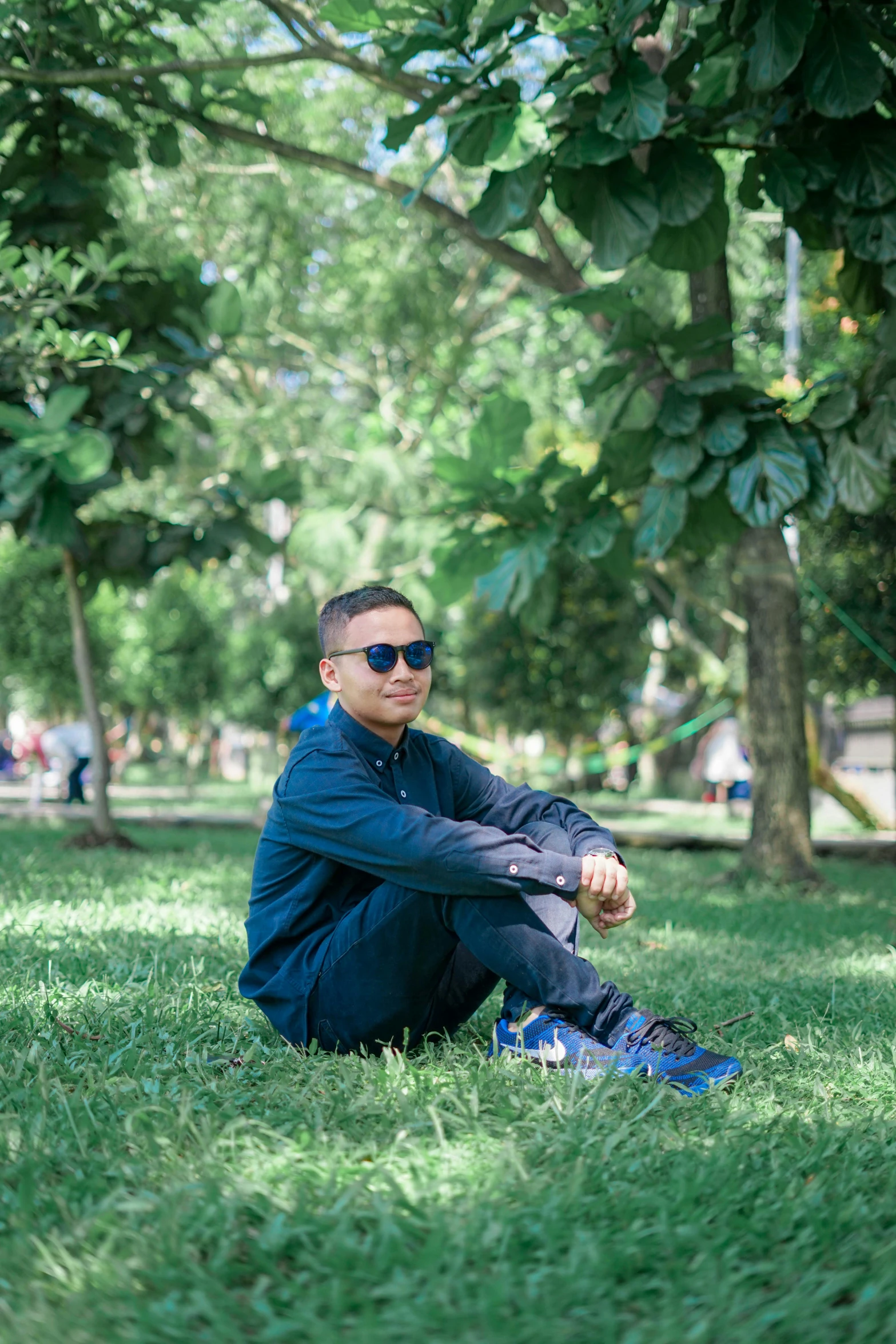 a man sitting on top of a lush green field, by Basuki Abdullah, wearing shades, city park, avatar image, portait photo profile picture