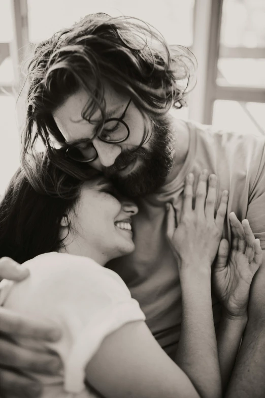 a black and white photo of a man hugging a woman, pexels contest winner, very attractive man with beard, wavy long black hair and glasses, happy vibes, 256435456k film