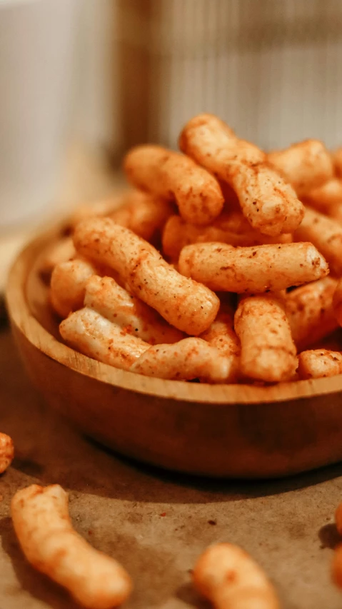 a wooden bowl of cheetos in front of some fried food