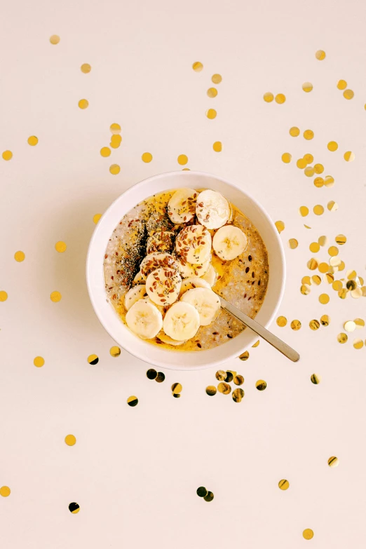 a bowl of oatmeal topped with banana slices, by Nicolette Macnamara, trending on pexels, confetti, gold glow, thumbnail, petite