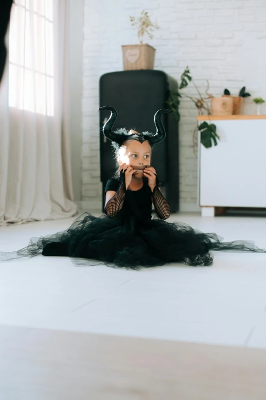 a little girl sitting on the floor with a sparkler in her hand, with black horns instead of ears, she is wearing a black dress, big natural horns on her head, profile image
