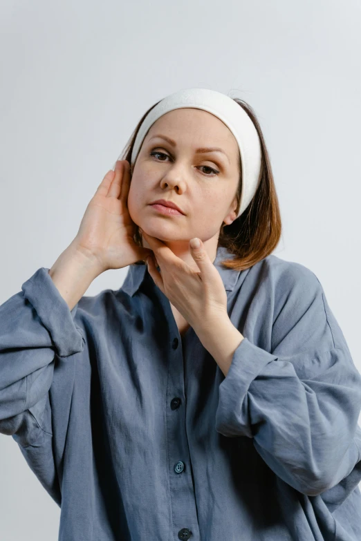 a woman in a blue shirt and a white headband, by Adam Marczyński, trending on pexels, renaissance, hands on face, pronounced facial contouring, in white turtleneck shirt, mid - 3 0 s aged