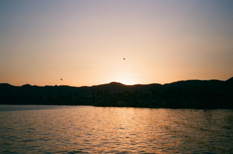 the sun is setting over a body of water, pexels contest winner, hills in the background, manly, sunfaded, medium format. soft light