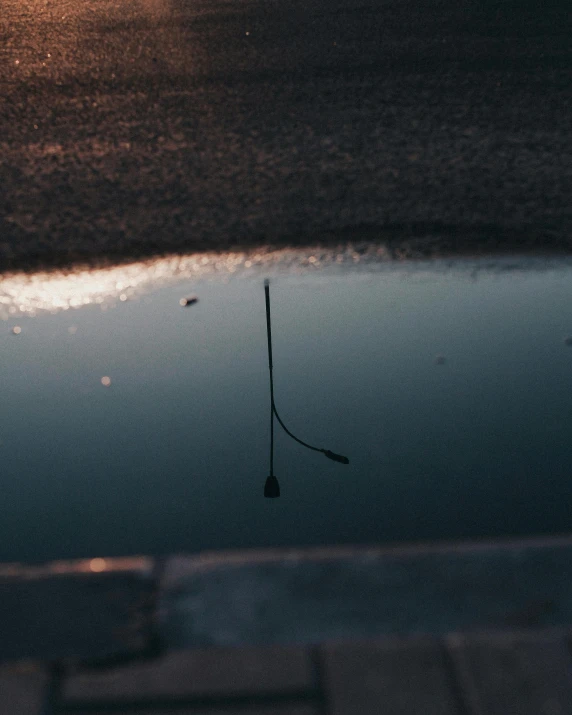 a puddle of water sitting on the side of a road, an album cover, unsplash, postminimalism, fishing pole, low quality photo, calm evening, in a pond