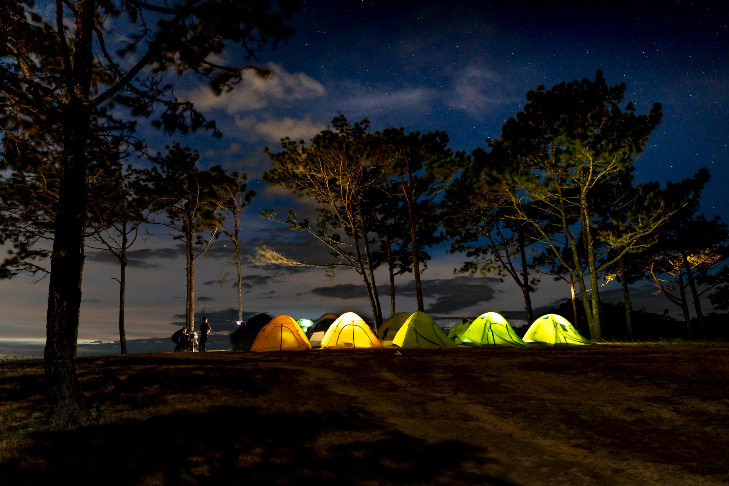 a group of tents sitting on top of a dirt field, by Julia Pishtar, pexels contest winner, neon lights lots of trees, standing near the beach, group of seven, slide show