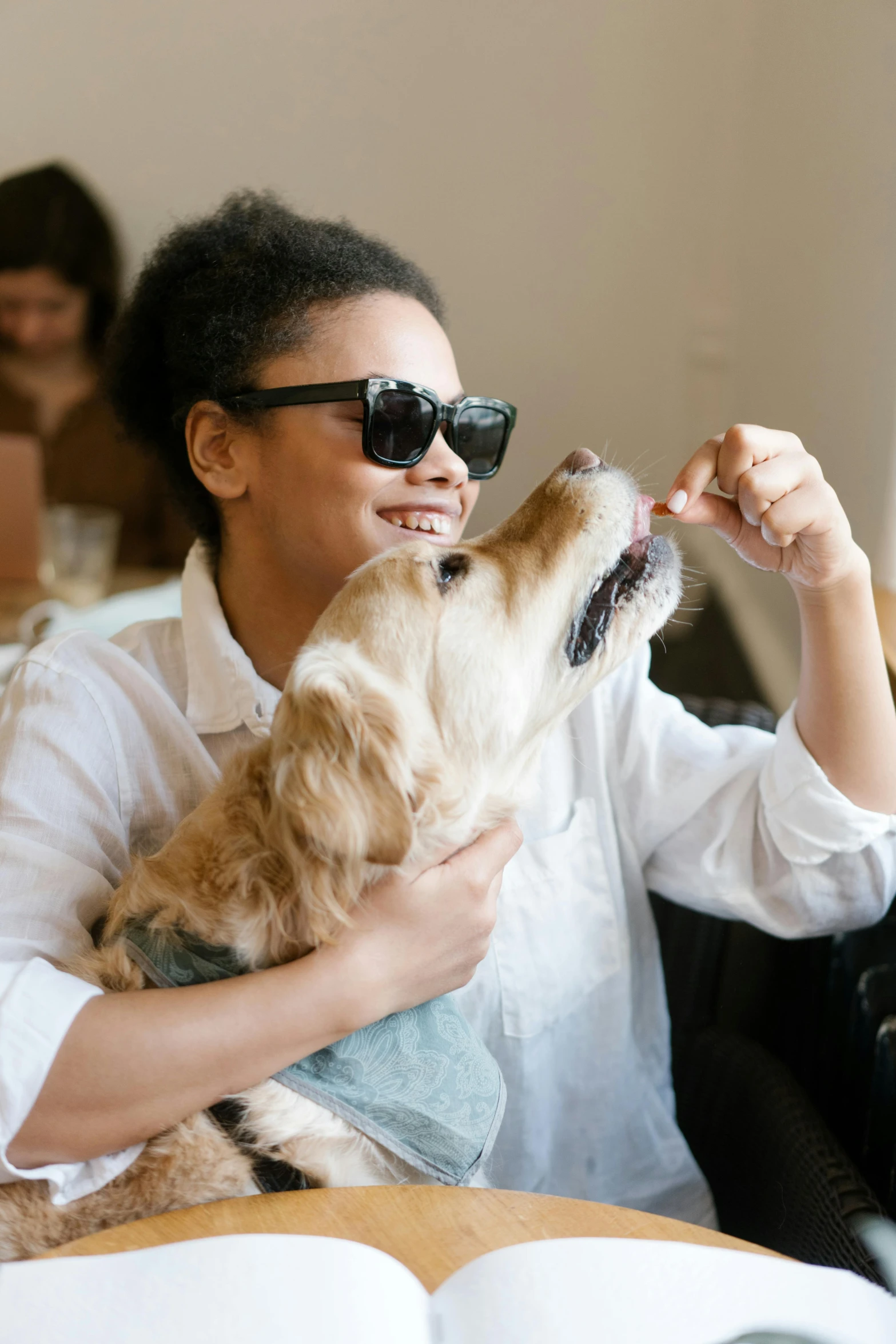 a woman sitting at a table with a dog, trending on unsplash, implanted sunglasses, anthropomorphic dog eating, woman holding another woman, tessa thompson