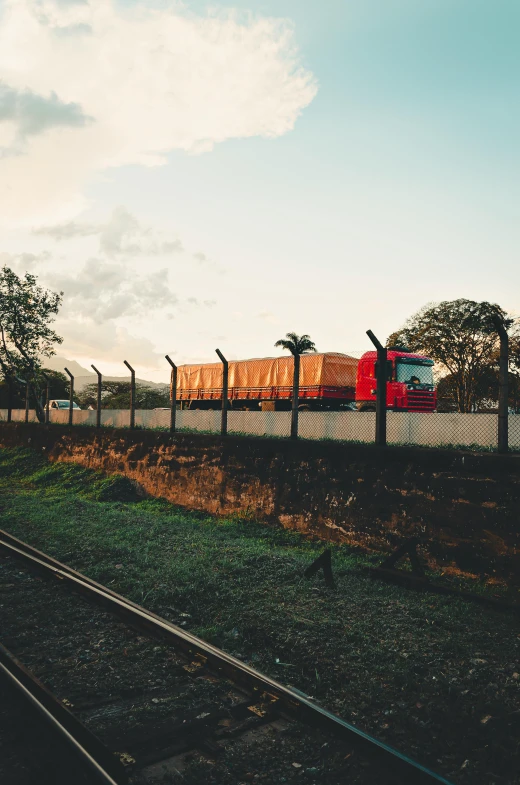 a train traveling down train tracks next to a lush green field, trading depots, sun setting, colombian, truck