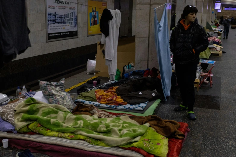 a man standing next to a pile of blankets, a photo, subway station, beds, contain, ap