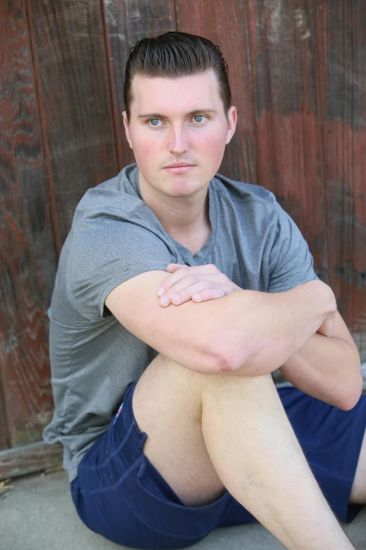 a young man sits against a wood background