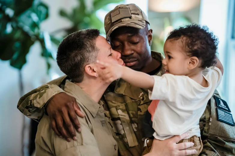 a man holding a small child in his arms, by Dan Frazier, pexels contest winner, wearing military outfit, two men hugging, lgbt, at home