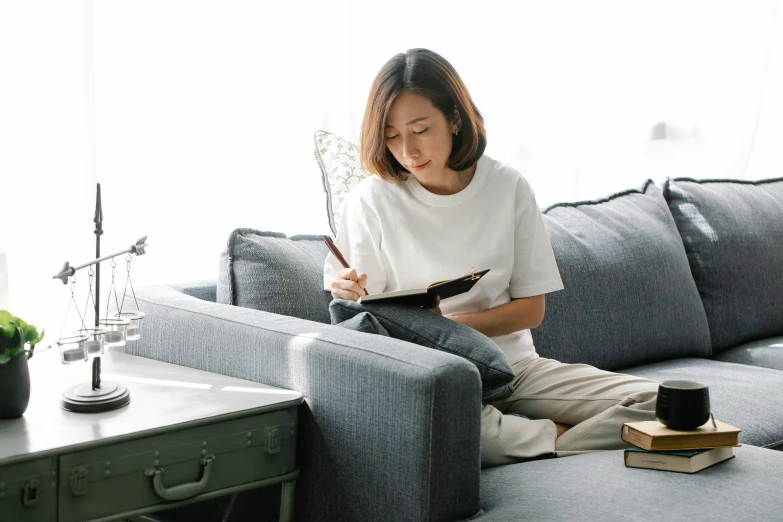 a woman sitting on a couch reading a book, inspired by Ruth Jên, pexels contest winner, happening, writing on a clipboard, grey, jia ruan, white l shaped couch