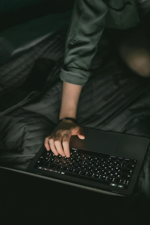 a person using a laptop on a bed, black on black, hunting, lit from above, keyboard