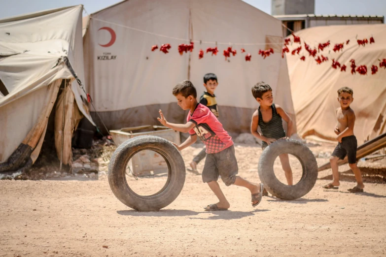 a group of children playing with a tire, by Dietmar Damerau, pexels contest winner, hurufiyya, camps in the background, real life photo of a syrian man, red cross, 🦑 design