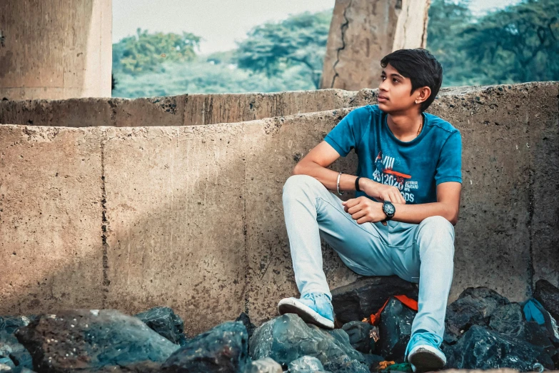 a young man sitting on top of a pile of rocks, pexels contest winner, realism, jayison devadas, innocent look, background image, sitting under bridge