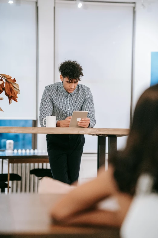 a man standing at a table with a tablet in front of him, trending on pexels, people sitting at tables, ignant, office clothes, ben mauro