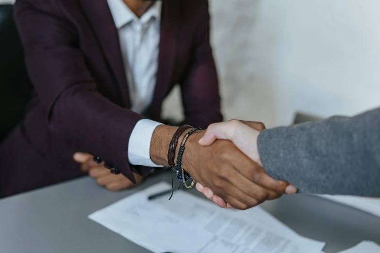 two people shaking hands across a table with papers on it