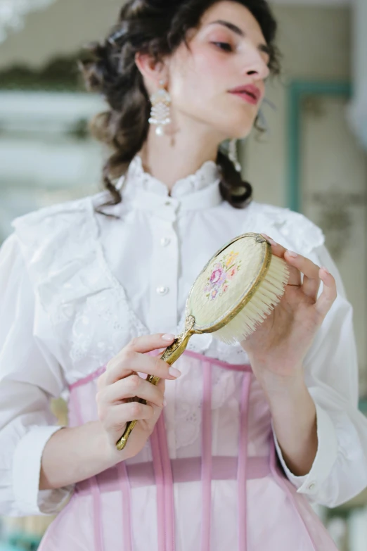 a woman is brushing her hair with a brush, inspired by Adélaïde Labille-Guiard, pexels contest winner, rococo, embroidered shirt, white and pink, detailed product shot, wearing victorian clothes