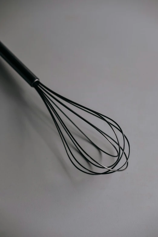 a whisk sitting on top of a white counter, pexels, black sokkel, on grey background, made of glazed, whips