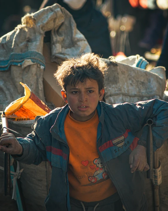 a young boy standing next to a pile of bags, by Youssef Howayek, pexels contest winner, happening, award winning movie still, rugged face, prideful look, in front of a large crowd