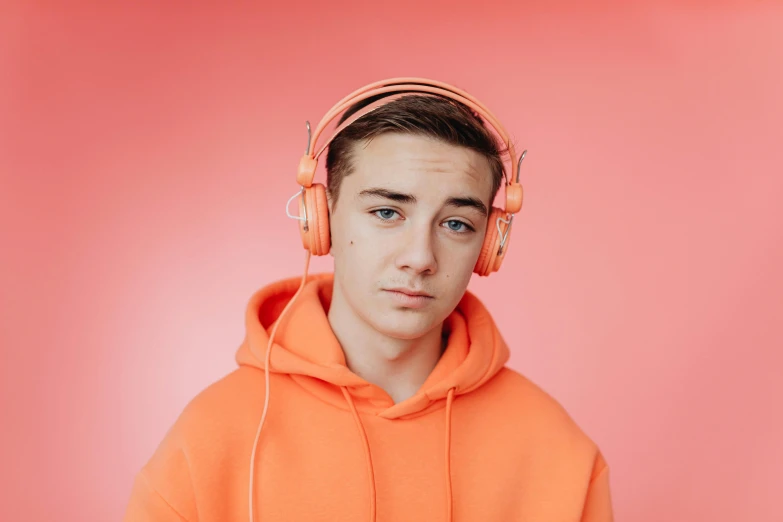 a man in an orange hoodie with headphones on, trending on pexels, hyperrealism, wearing a pastel pink hoodie, twink, irish youtuber, connor hibbs